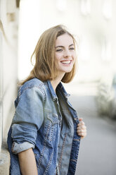 Porträt einer lächelnden jungen Frau vor einer Hausfassade - MAEF12438