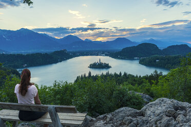 Slowenien, Bled, Junge Frau bewacht die Insel Bled und die Kirche Maria Himmelfahrt bei Sonnenaufgang - LOMF00623