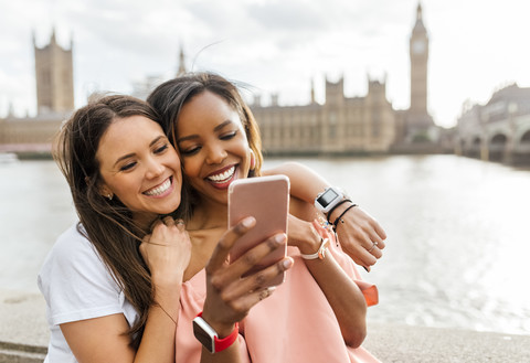 UK, London, two happy women with smartphone near Westminster Bridge stock photo