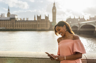 UK, London, Frau sendet Nachrichten mit ihrem Smartphone in der Nähe der Westminster Bridge - MGOF03639