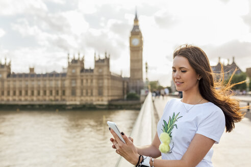 UK, London, Frau sendet Nachrichten mit ihrem Smartphone auf der Westminster Bridge - MGOF03652