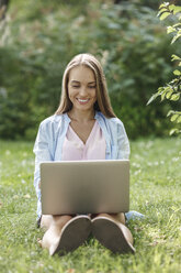 Smiling young woman using laptop on a meadow - VPIF00140