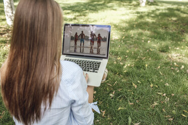 Junge Frau betrachtet auf einer Wiese eine Fotografie auf einem Laptop-Bildschirm - VPIF00141