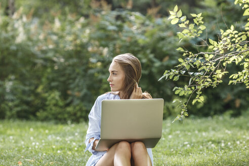 Junge Frau mit Laptop auf einer Wiese mit Blick zur Seite - VPIF00142