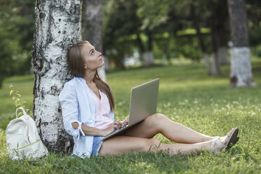 Junge Frau mit Laptop auf einer Wiese mit Blick nach oben - VPIF00145