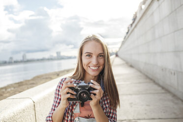 Smiling young woman with a camera at the riverside - VPIF00161