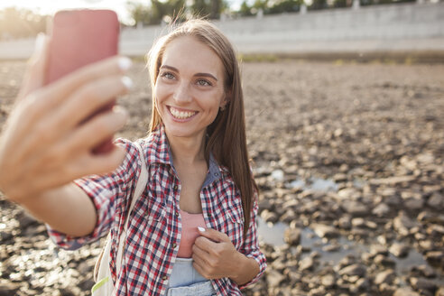 Porträt einer glücklichen jungen Frau am Flussufer, die mit ihrem Handy telefoniert - VPIF00174