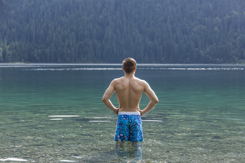 Deutschland, Bayern, Eibsee, Rückenansicht eines im Wasser stehenden jungen Mannes, lizenzfreies Stockfoto