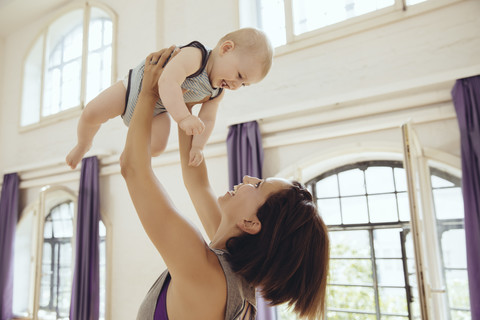 Sporty woman lifting up happy baby in training room stock photo