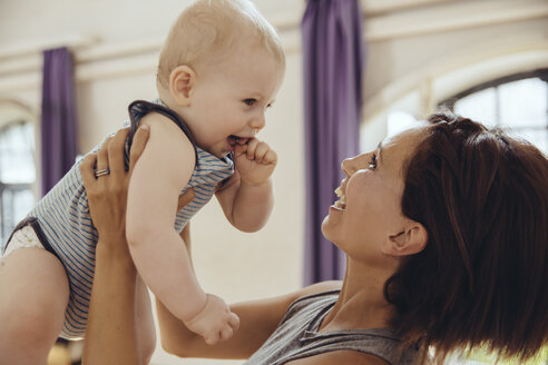 Sportliche Frau hebt glückliches Baby im Trainingsraum hoch - MFF03997