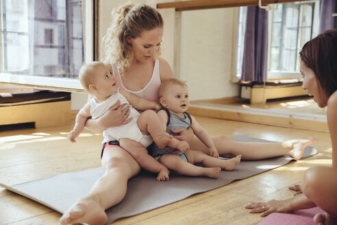 Mutter mit Zwillingsbabys auf Yogamatte sitzend - MFF03999