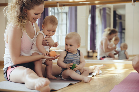 Mutter mit spielenden Zwillingsbabys auf Yogamatte sitzend, lizenzfreies Stockfoto