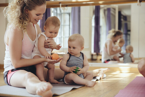 Mutter mit spielenden Zwillingsbabys auf Yogamatte sitzend - MFF04000