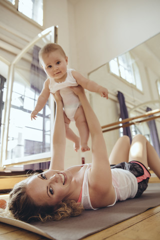 Mutter trainiert auf einer Yogamatte, während sie ihr Baby hochhält, lizenzfreies Stockfoto