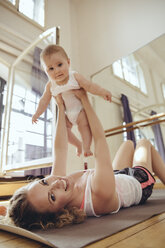 Mother working out on yoga mat while holding up her baby - MFF04002