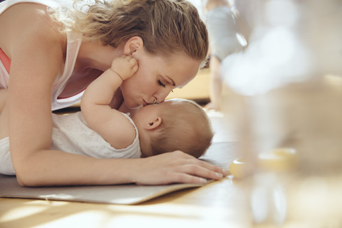 Mutter küsst ihr Baby beim Training auf einer Yogamatte, lizenzfreies Stockfoto