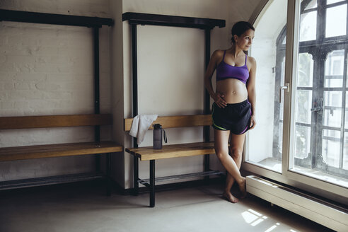 Sportliche schwangere Frau steht in der Umkleidekabine und schaut aus dem Fenster - MFF04036