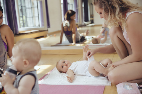 Mother changing diapers of baby in exercise room stock photo