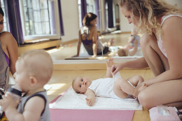 Mother changing diapers of baby in exercise room - MFF04046