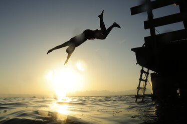 Man jumping fom jetty into the sea at sunset - ECPF00133