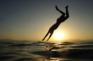 Mann springt bei Sonnenuntergang ins Meer - ECPF00134