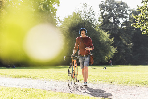 Mann mit Rennrad hört Musik mit Kopfhörern in einem Park, lizenzfreies Stockfoto