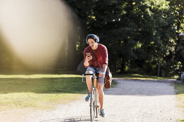 Mann auf Rennrad mit Blick auf Handy in einem Park - UUF11744