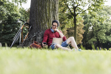 Man using laptop and cell phone in park - UUF11746