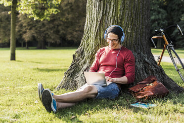 Mann mit Laptop und Kopfhörern im Park - UUF11749