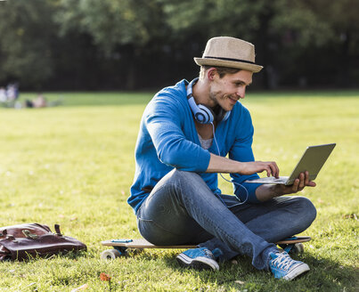 Mann mit Skateboard benutzt Laptop im Park - UUF11757