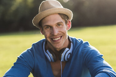 Porträt eines lachenden Mannes mit Hut und Kopfhörern in einem Park - UUF11759