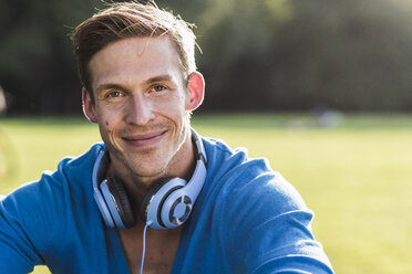 Porträt eines lächelnden Mannes mit Kopfhörern in einem Park - UUF11760