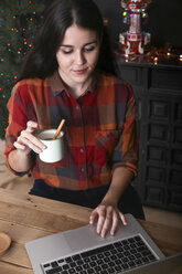 Lächelnde Frau mit einer Tasse Kaffee am Laptop zur Weihnachtszeit - RTBF01021