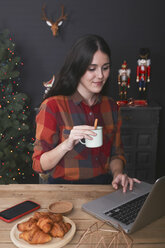 Lächelnde Frau mit einer Tasse Kaffee am Laptop zur Weihnachtszeit - RTBF01022