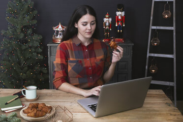 Junge Frau benutzt einen Laptop und isst ein Croissant zur Weihnachtszeit - RTBF01024