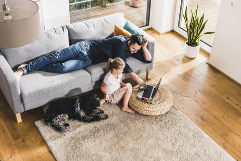 Father using laptop at home with his little daughter stock photo