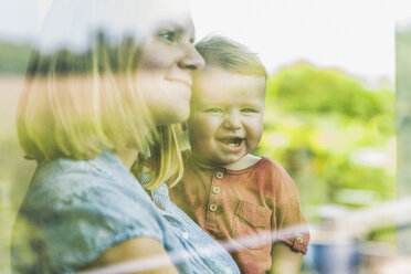 Mother looking out of window, with son on her arm - UUF11790