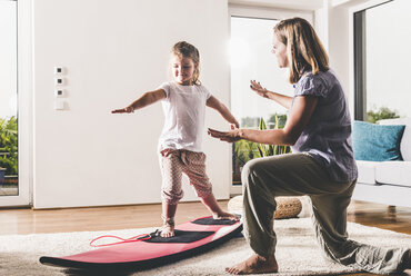 Mutter und Tochter trainieren mit Surfbrett im Wohnzimmer - UUF11804