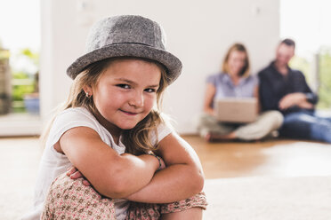 Little girl with hat, parents using laptop in background - UUF11814