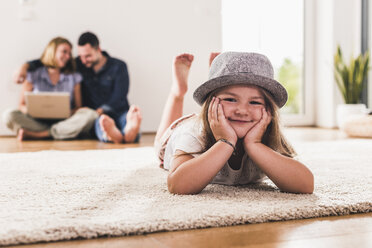 Little girl with hat having fun at home, parents using laptop in background - UUF11816