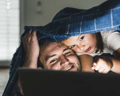 Happy family hiding under blanket, watching film on laptop - UUF11823