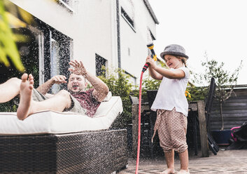 Vater und Tochter im Garten, Tochter spritzt mit dem Schlauch Wasser - UUF11829