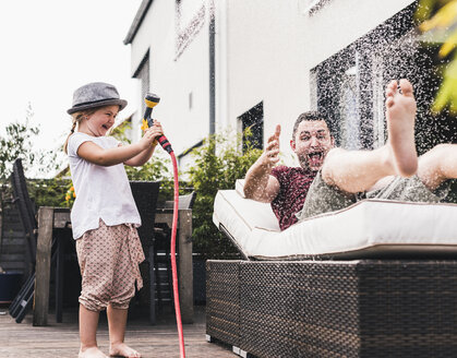 Vater und Tochter im Garten, Tochter spritzt mit dem Schlauch Wasser - UUF11830