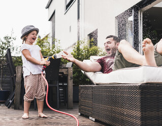 Fathercand daughter in the garden, daughter splashing water with hose - UUF11831