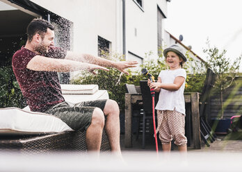 Vater und Tochter im Garten, Tochter spritzt mit dem Schlauch Wasser - UUF11832