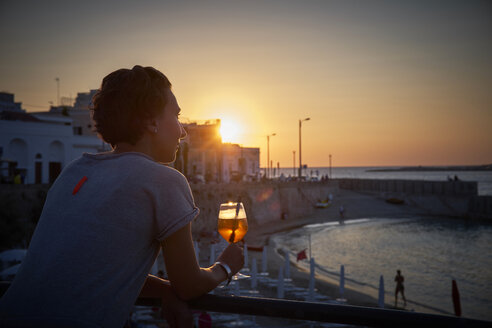 Italien, Santa Maria al Bagno, Frau entspannt sich mit einem Glas Spritz bei Sonnenuntergang - DIKF00269