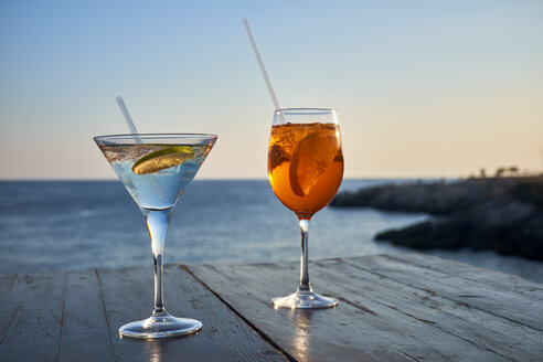 Ein Glas eisgekühlter Spritz mit Orangenscheibe und ein Glas Martini mit Limettenscheibe vor dem Meer - DIKF00270