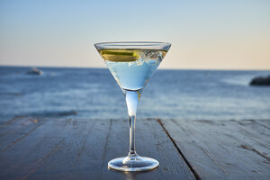 Ein Glas eisgekühlter Martini mit Limettenscheibe vor dem Meer - DIKF00271