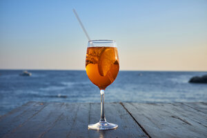 Ein Glas eisgekühlter Spritz mit Orangenscheibe vor dem Meer - DIKF00272