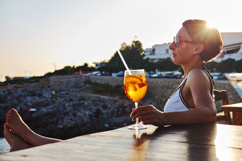 Italien, Santa Caterina, Frau entspannt sich auf der Promenade mit einem Glas Spritz bei Sonnenuntergang - DIKF00273